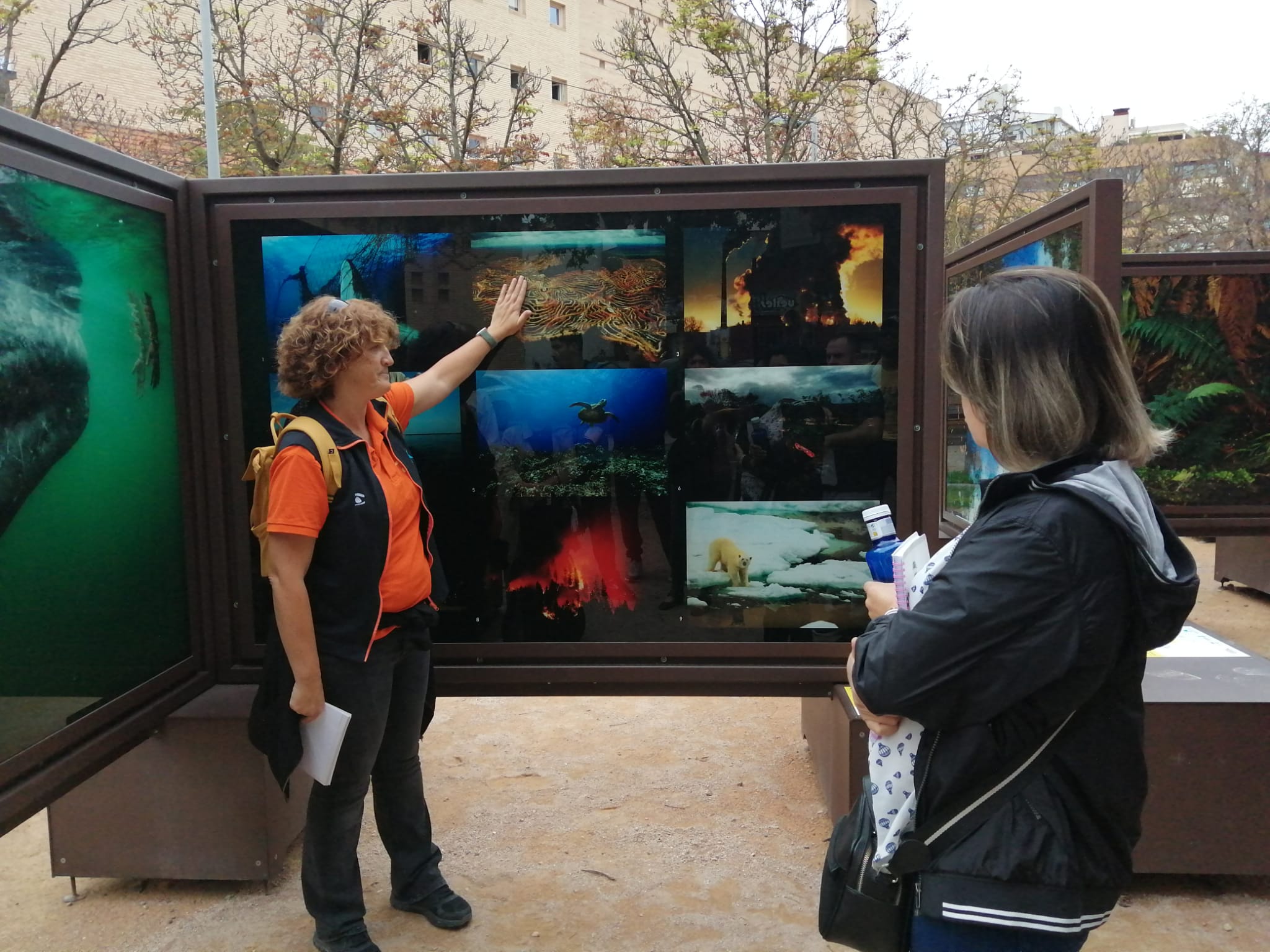 Guía de la exposición explicando la imágenes mientras que una de las alumnas asistentes escucha la explicación.